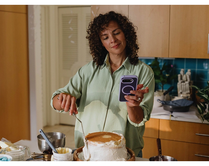 Woman checks her phone while frosting a cake in a her kitchen.