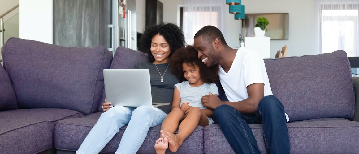 Young family searching online for home on sectional couch.