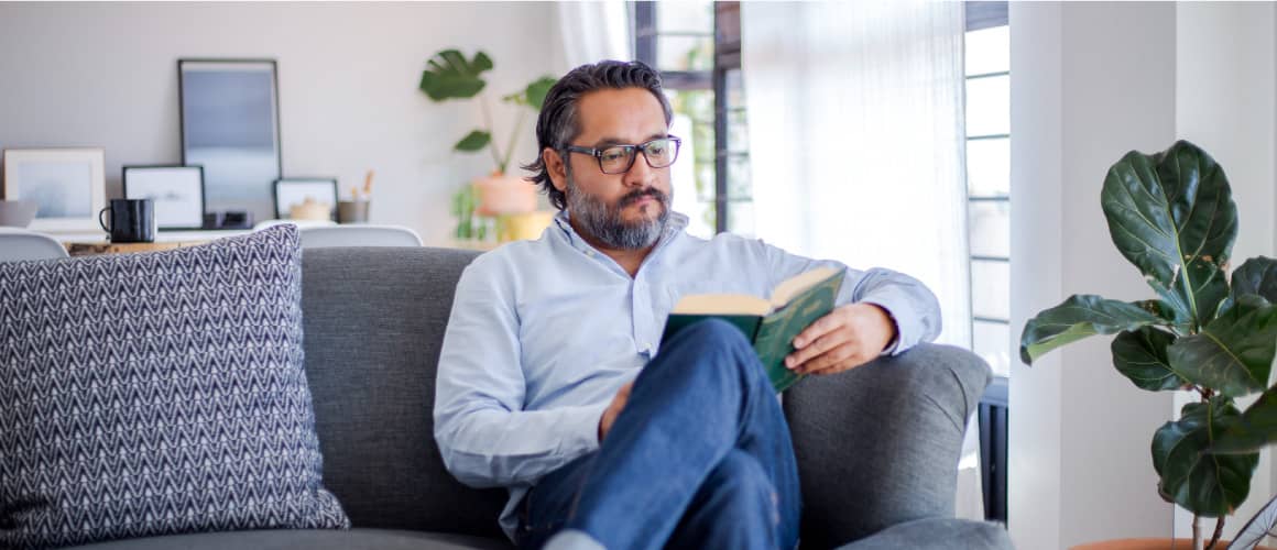 Man reading an investment strategy book on couch in living room.