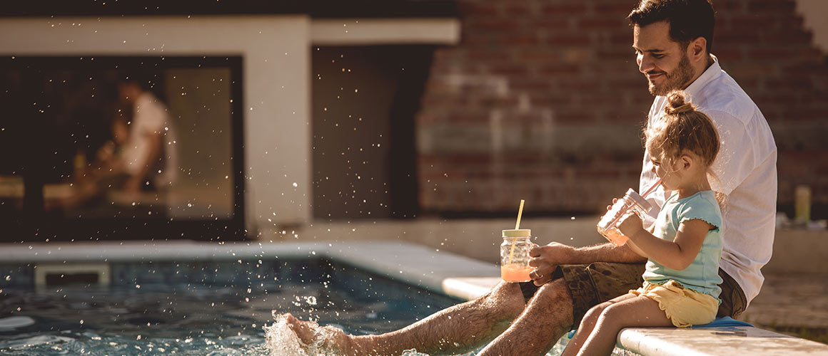 Father and daughter sitting by their pool of their vacation home.