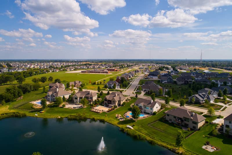 Rural neighborhood in Bettendorf, IA, with large, green yards, swimming pools and lake with fountain.