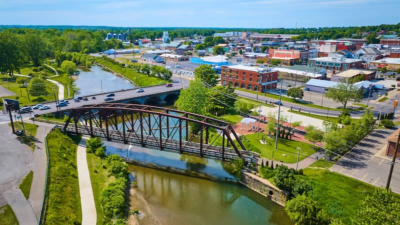 Cement bridge and old rail bridge crossing over river and commercial buildings in background of Mount Vernon, OH.