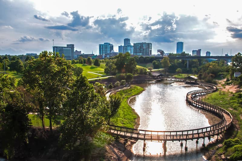 View of Riverfront Park in Little Rock, with bridged trail around river and skyline in background.