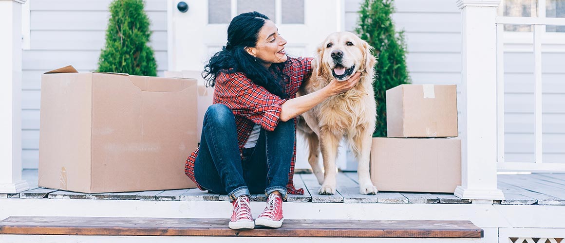 Woman and her dog sitting on porch with moving boxes.