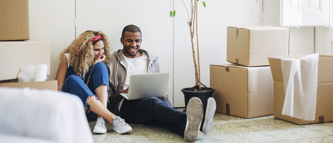 Couple sitting on floor with laptop surrounded by moving boxes