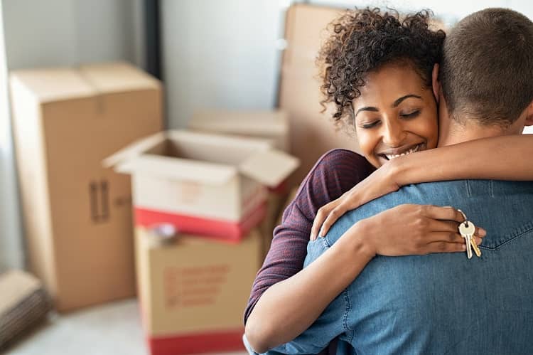 Happy couple hugging with house keys and moving boxes around