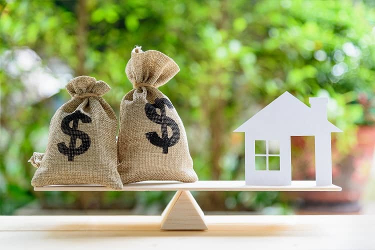 House figurine and money balancing on a teeter totter