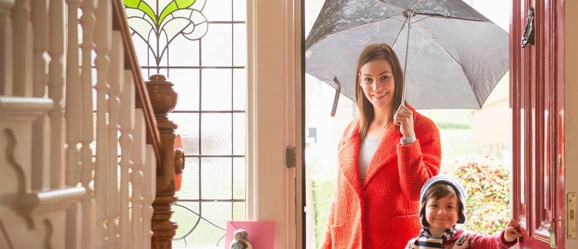 Mother in red coat with umbrella entering doorway with son.