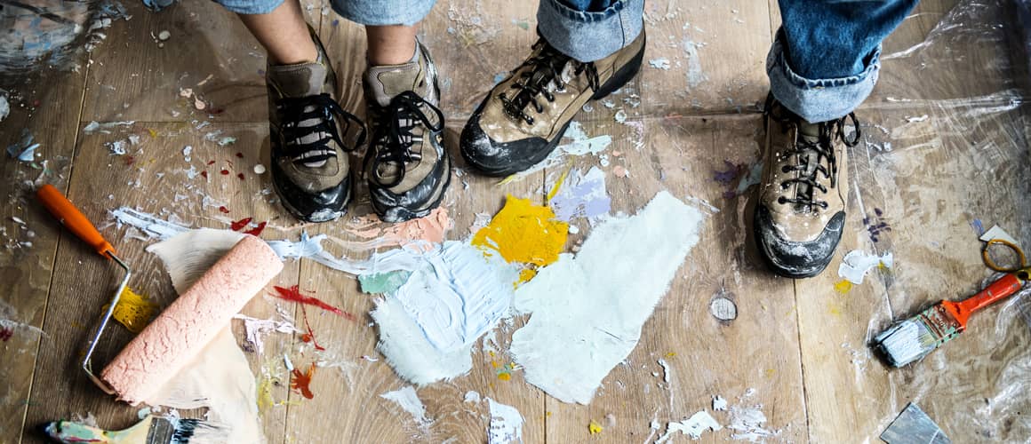 Two people's feet with paint brush and paint on floor
