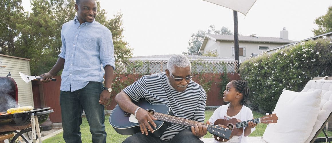 Family on the patio grilling and playing guitar. Grandparent, father and daughter.