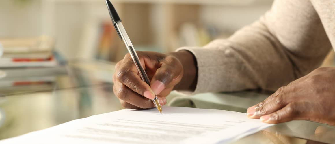 Black Man Hands Signing Document On A Desk At Home