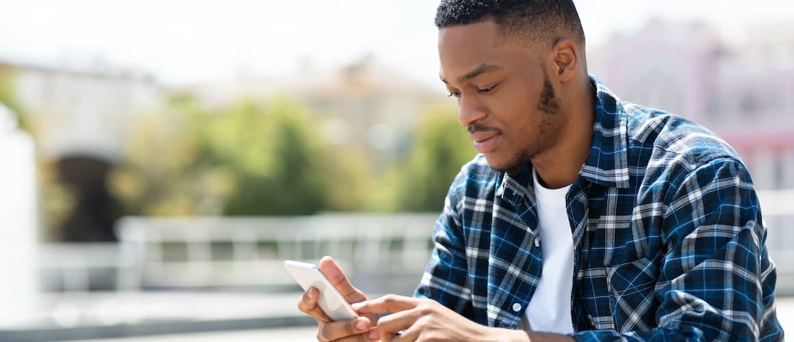 African American man looking at phone in blue plaid shirt on a sunny day.