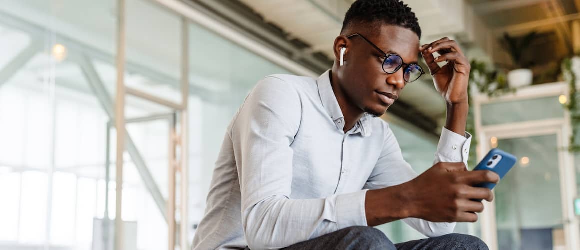 Black Man Sitting In A Glass Building Looking At His Phone