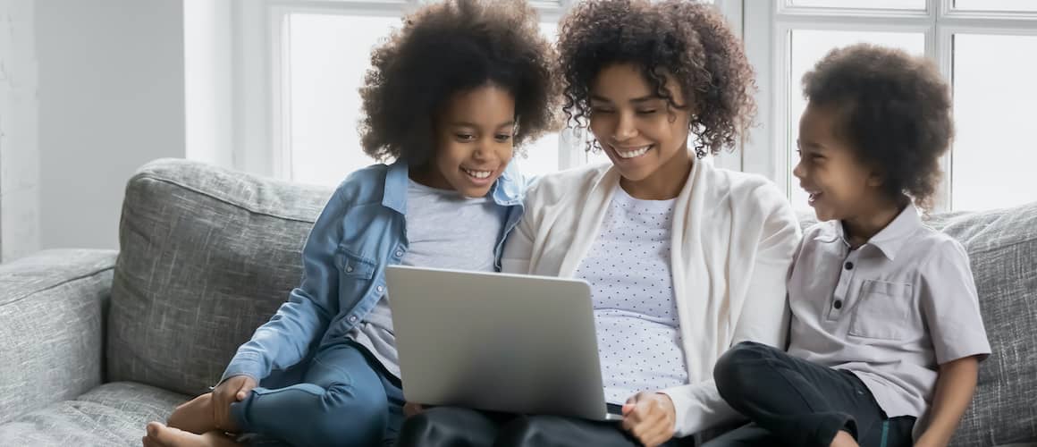 Black Woman With Two Daughters On Couch Looking At Computer