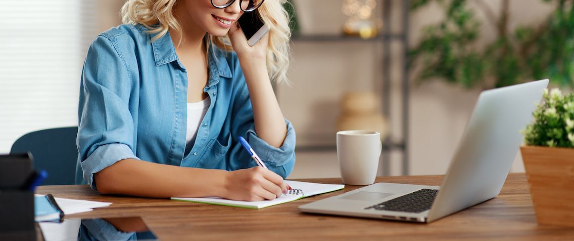 Blonde woman writing notes while on the phone.