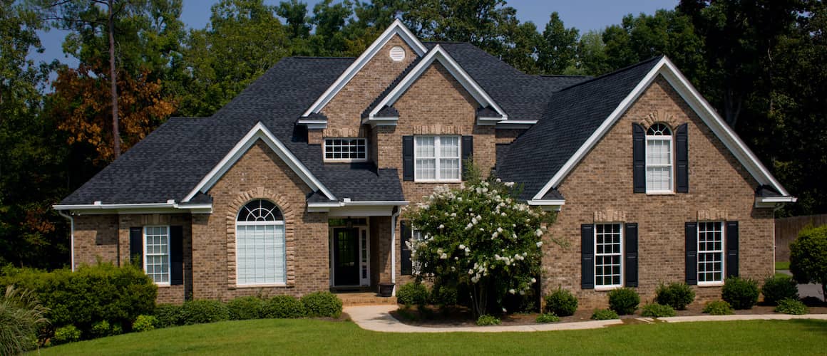 Brown Brick House With Black Roof And Shudders