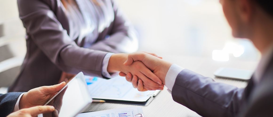 Business handshake happening across a table between two colleagues.