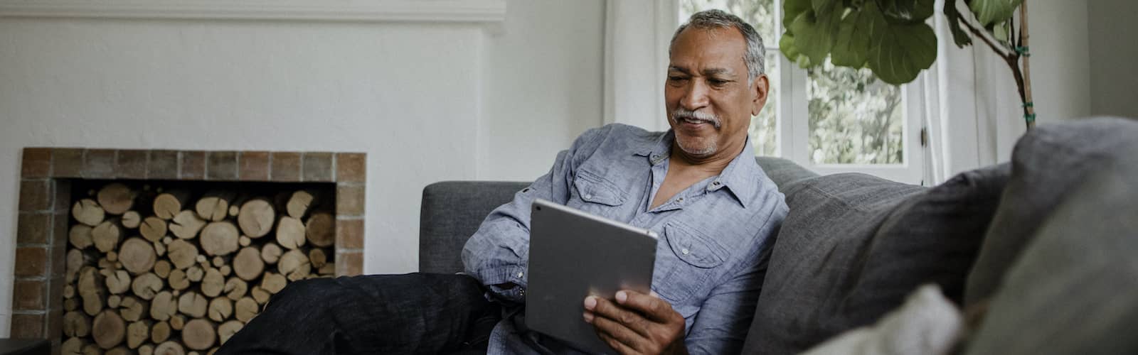 Older Hispanic man with large fiddle leaf house plant in background.