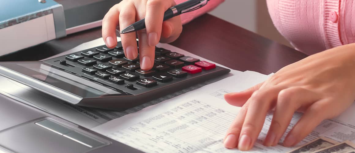 Close up view of a woman's hands using a calculator and looking over a document on a desk.