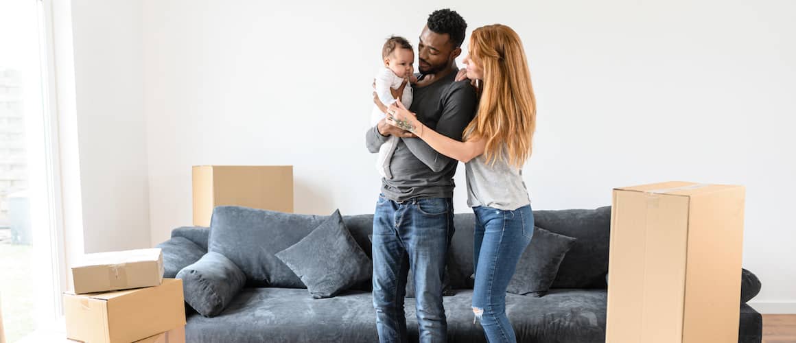 Young couple with their baby standing in a new, empty home with boxes.