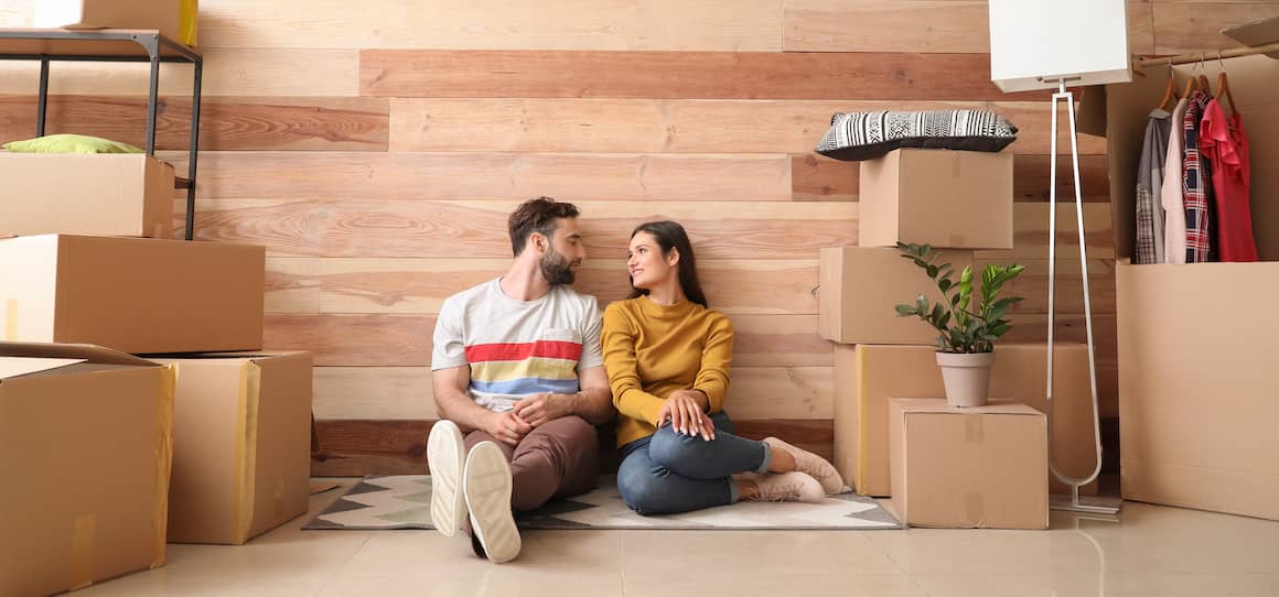 Couple sitting in their new house on the floor unpacking.