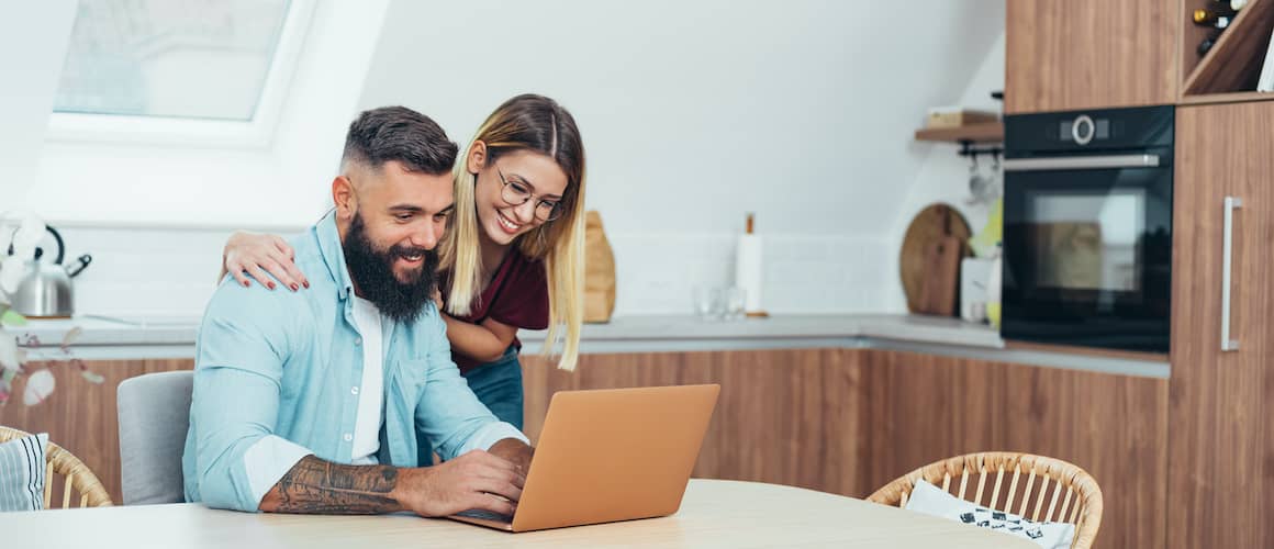 Couple researching at kitchen table on laptop.
