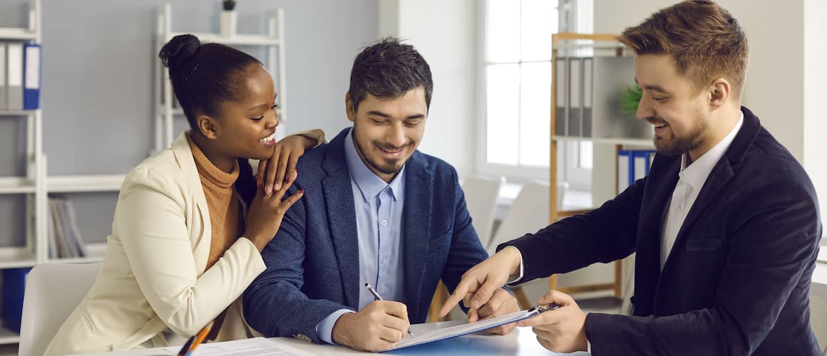 Couple signing documents with agent and smiling.