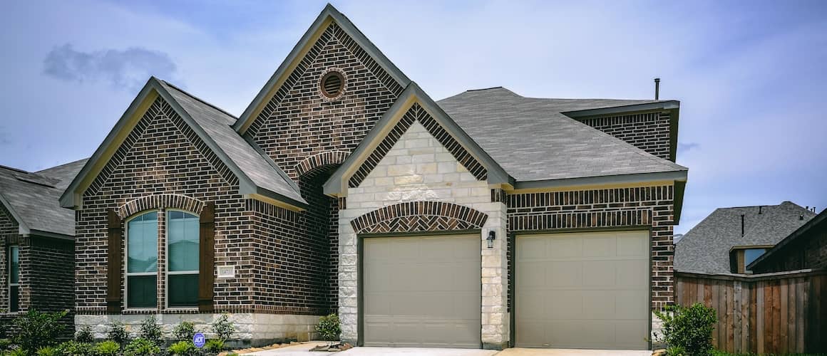 Dark brown and light brown specked brick home with white sand stone garage.
