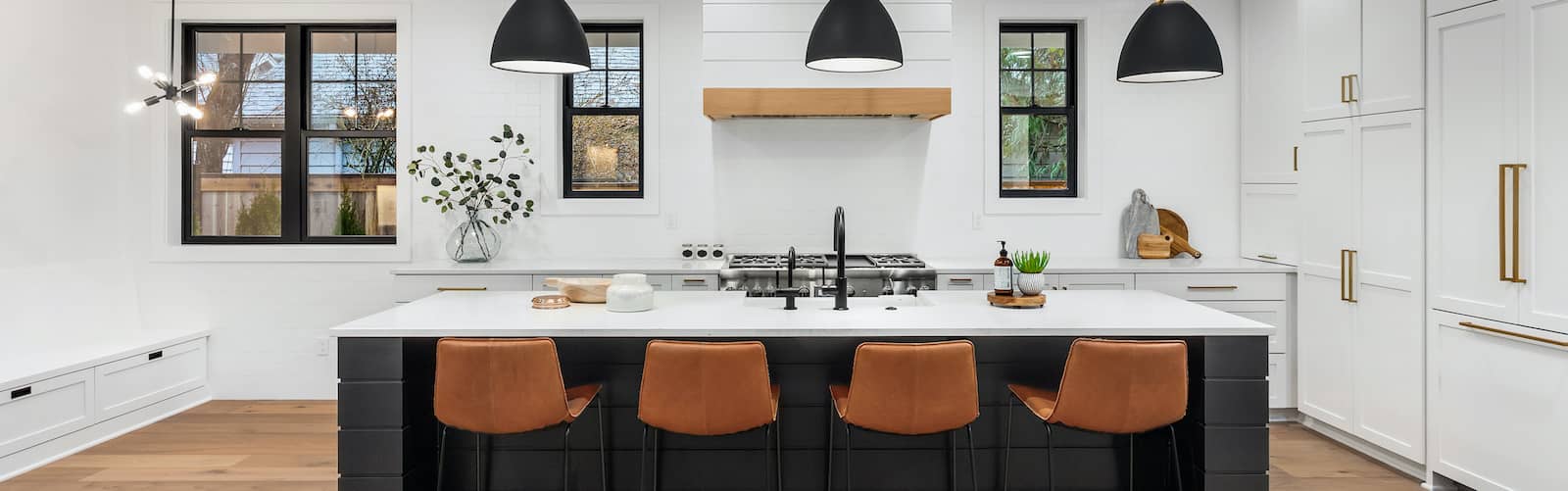 Remodeled white kitchen with black and gold finishes and brown leather bar stools.