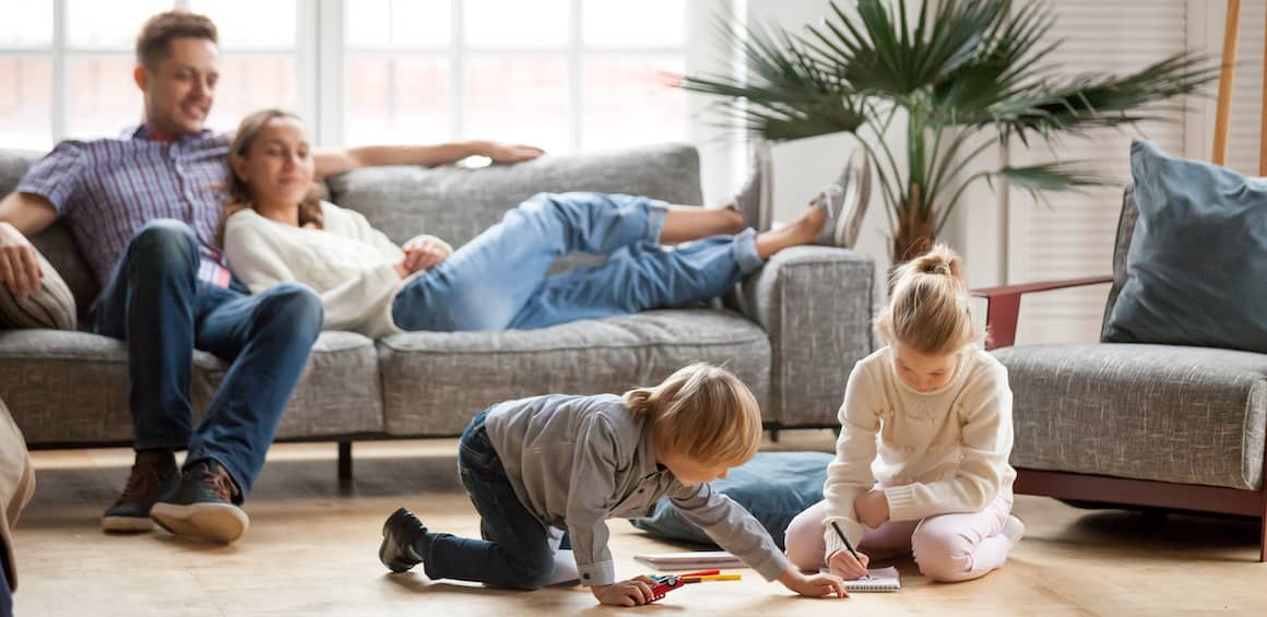 parents sitting on couch in their living room watching their two kids play on the floor