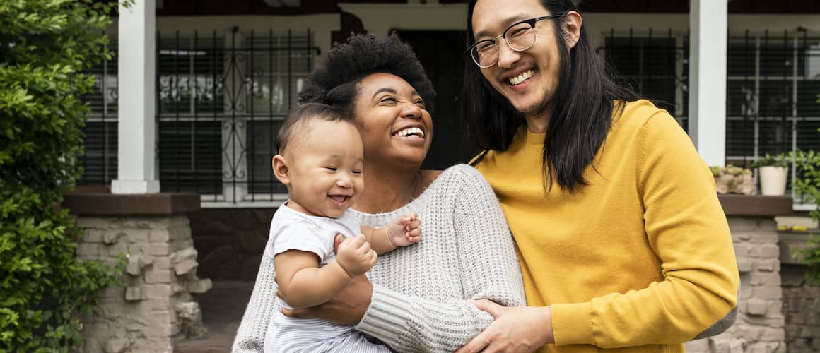 Family hugging in front of house and smiling.