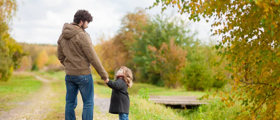 Father walking with young daughter along a dirt trail.