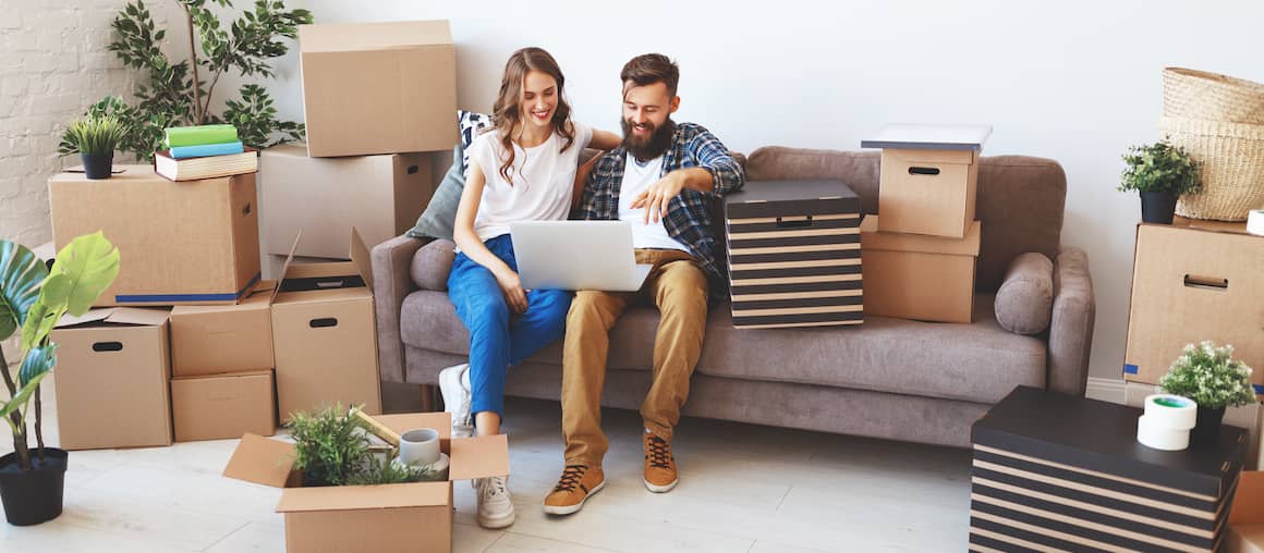 couple sitting in new home with moving boxes and looking online