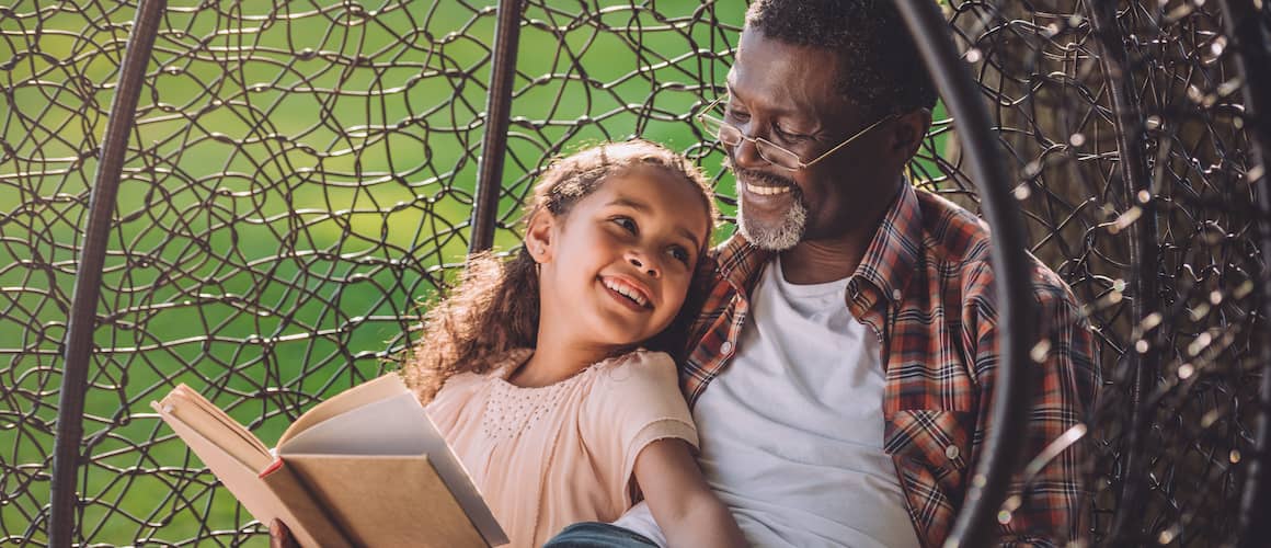 Grandfather And Grand Daughter Reading In Swinging Chair