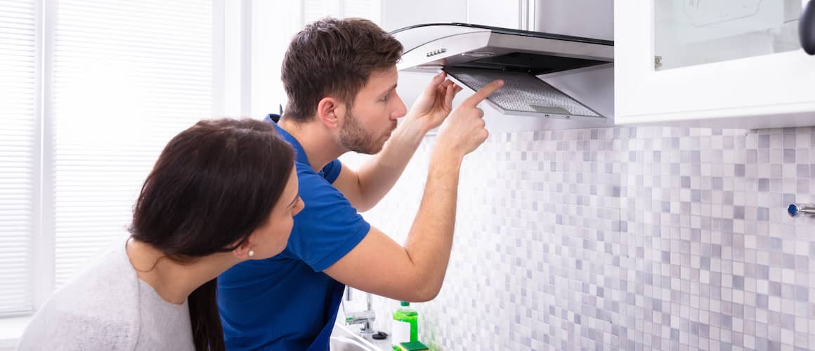 Woman watching man fix hood over stove.