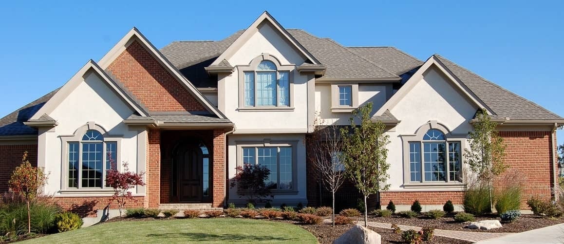 Large brick home in front of a blue sky.