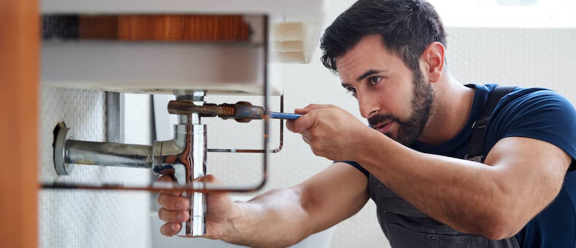 Plumber Using Wrench To Fix Leaking Sink In Home Bathroom