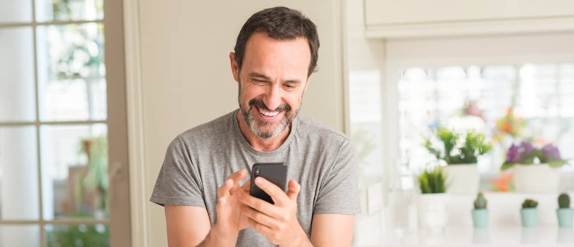 Man on his phone in his house with potted plants behind him.
