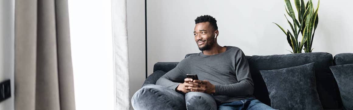 African American man on couch on airpods discussing refinance