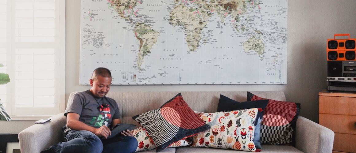 Man sitting on a couch with a world map behind him.