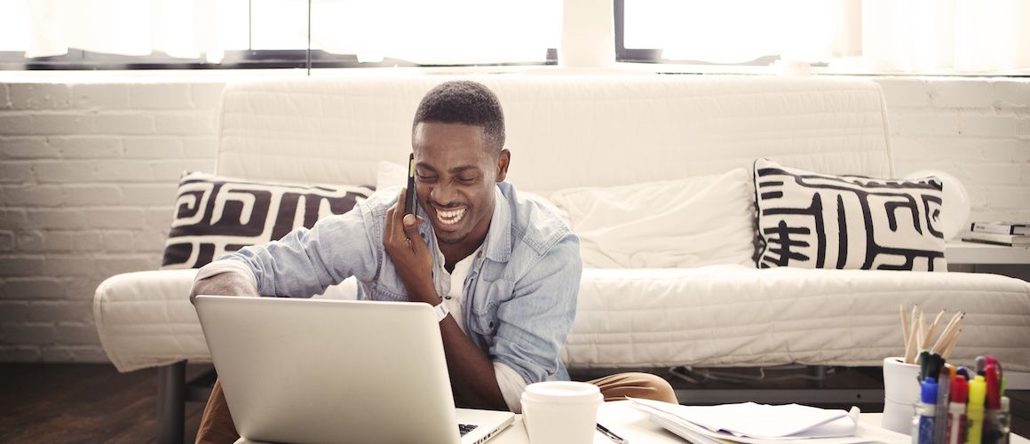 Smiling man talking on the phone while using his laptop.