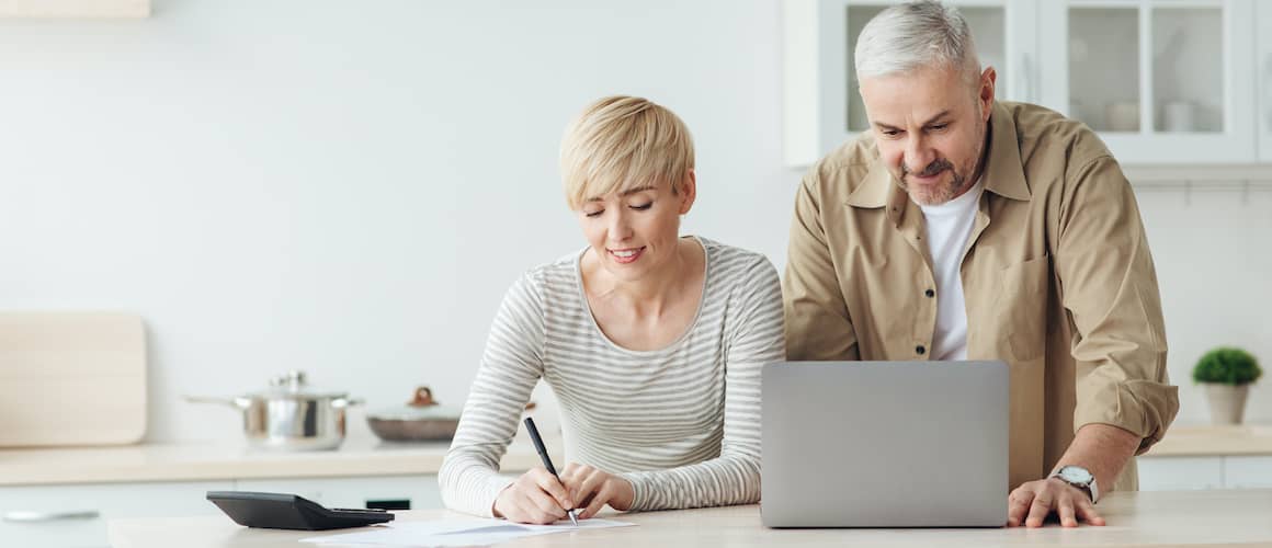 Middle aged couple at kitchen island on computer and calculator.