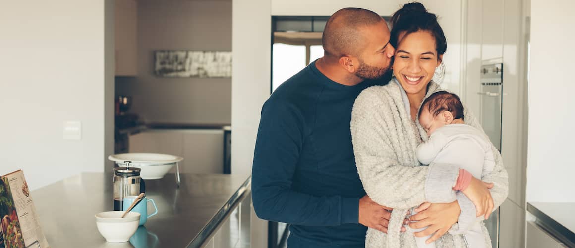 Family with new baby in kitchen of home deciding to refinance or modify home loan.