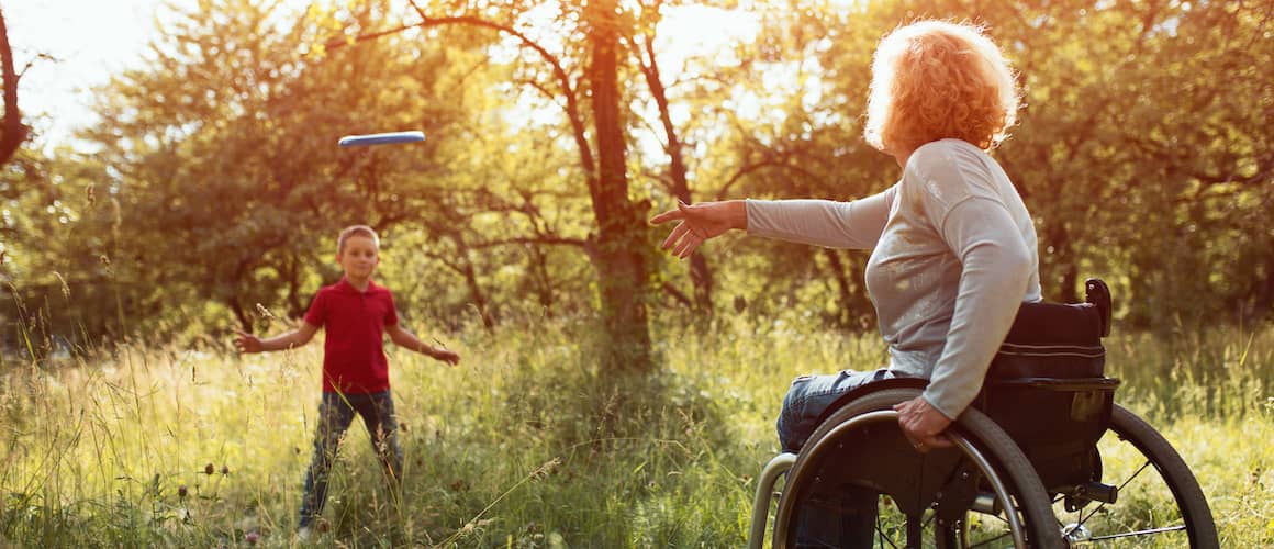 Mother in wheelchair playing frisbee outside with her son.