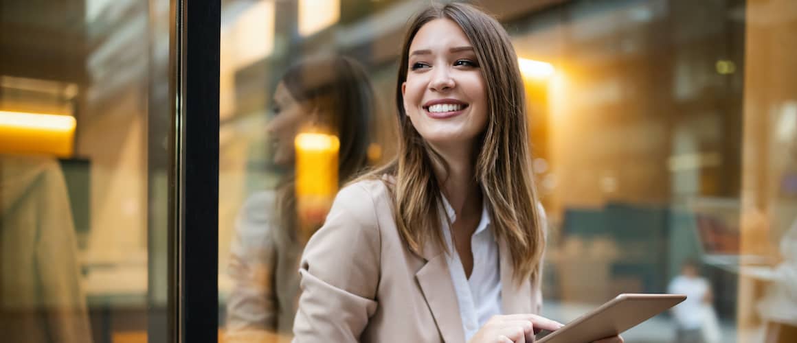 Woman smiling and holding an iPad in front of a clear window.