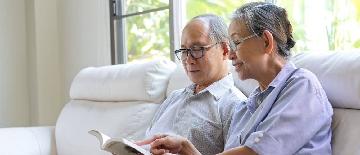 Older Asian couple reading together on their couch.