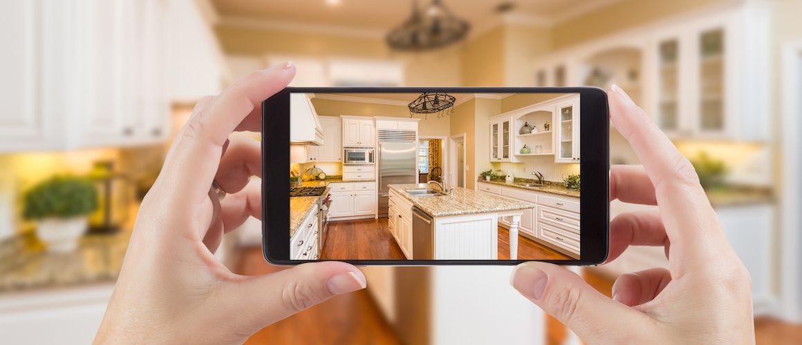 Woman holding up phone to take a picture of a kitchen.