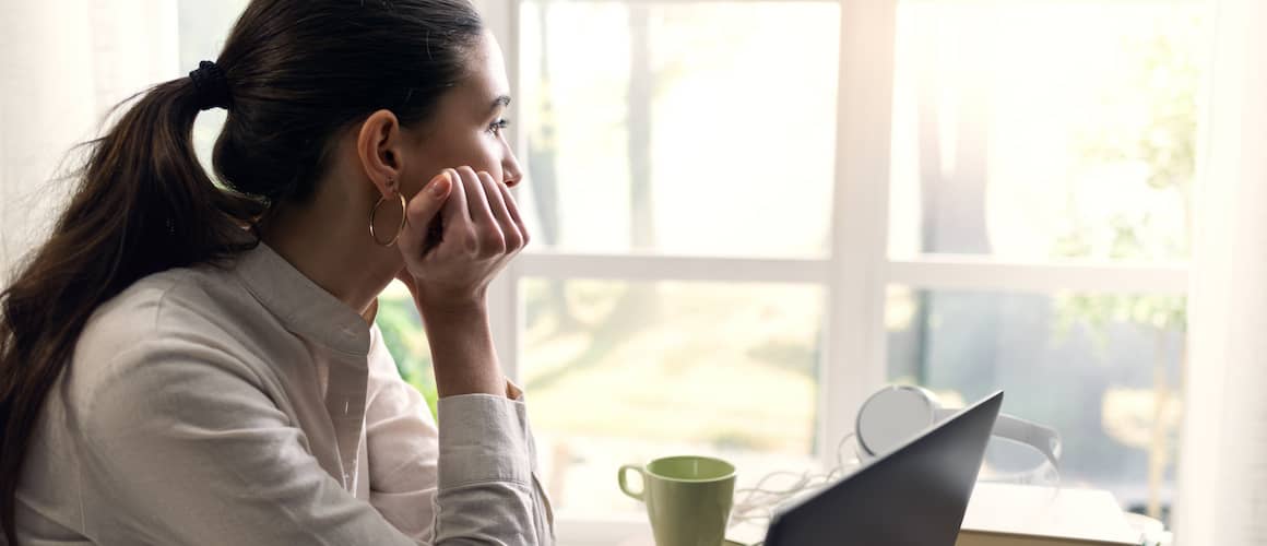 Woman looking outside window at home office desk.