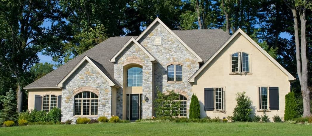 Stone-faced tan home that is newly built and surrounded by trees.