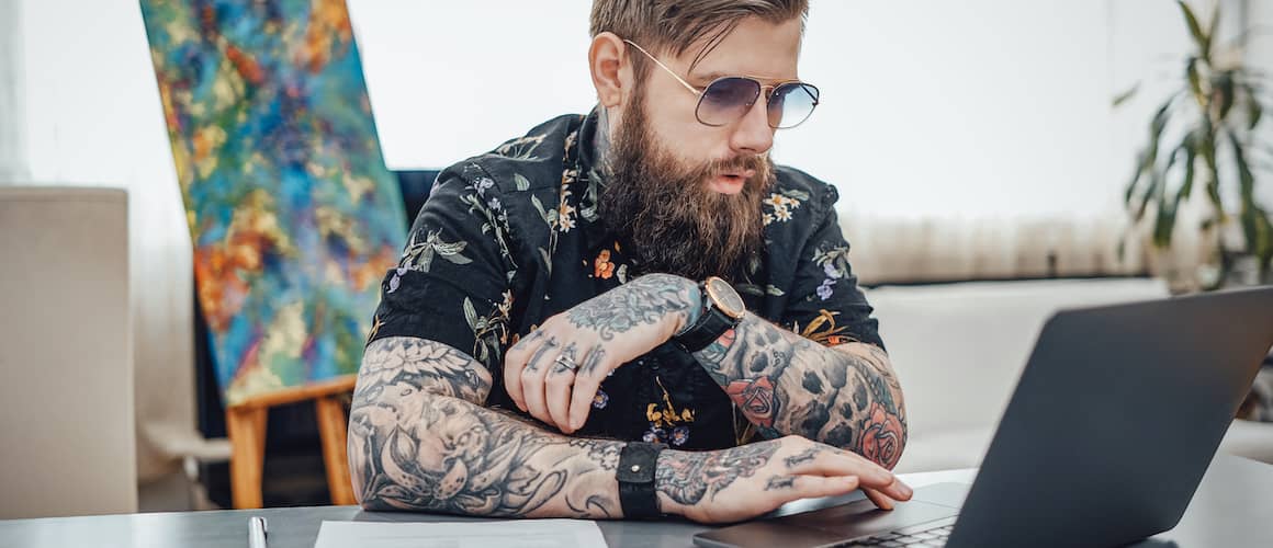 Stylish young man with tattoo sleeves working on computer.